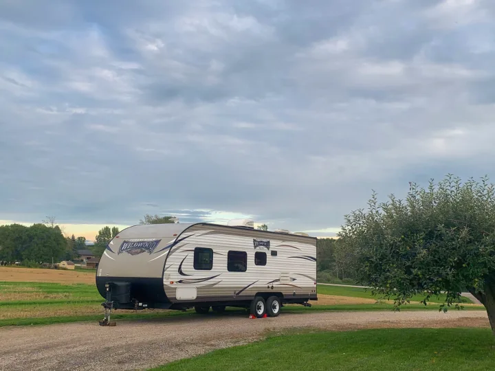 Experience rural charm with this RV rental. A Wildwood travel trailer parked by fields and an apple tree under a gray sky.. Forest River Wildwood X-Lite 2017
