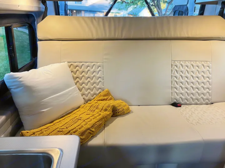 Relaxing RV rental interior: cream quilted bench seat, white pillow, yellow throw, and window view.. Winnebago Solis 2023