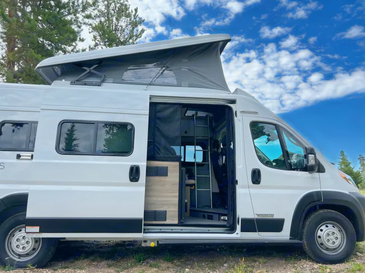 White Winnebago rv rental camper van with open side door, pop-top roof extended, parked for outdoor adventure.. Winnebago Solis 2023