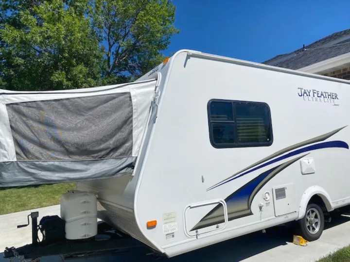 This white Jay Feather Ultra Lite RV rental features blue graphics, a pop-out canvas bunk, and a spare tire, ready for adventure.. Jayco Jay Feather Ultra Lite 2012