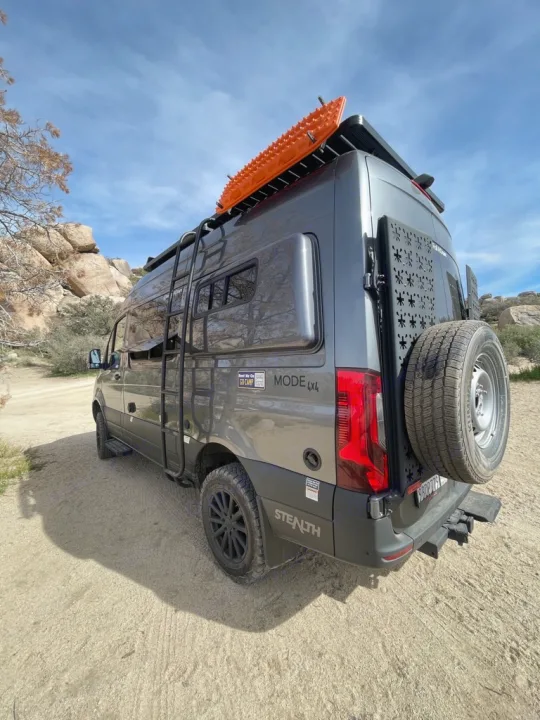A gray 4x4 Sprinter adventure van (rv rental) with roof rack, ladder, and spare tire, ready for off-road exploration.. Storyteller Overland Storyteller Overland Class B 2022