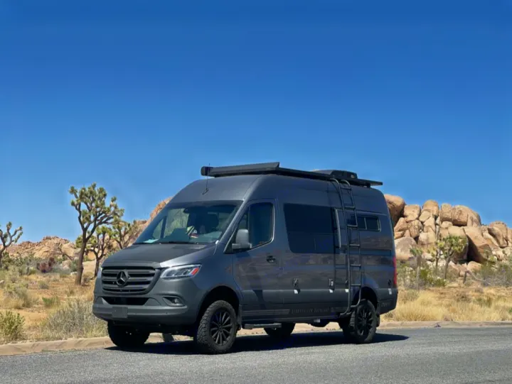 This grey Sprinter van RV rental is ready for desert adventures, parked among Joshua trees and rock formations.. Storyteller Overland Storyteller Overland Class B 2022