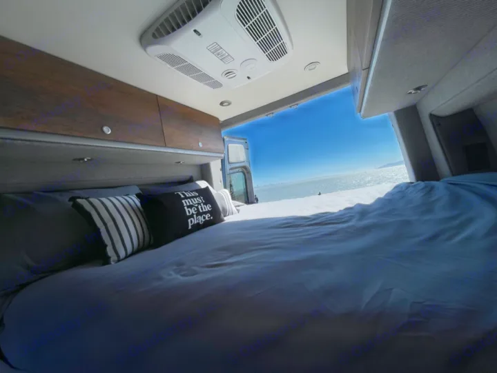 Cozy RV rental interior with a comfy bed offering breathtaking bay views from the open rear doors, perfect for relaxing travel.. Storyteller Overland Storyteller Overland Class B 2022
