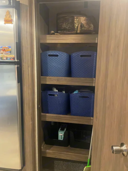 An RV rental's organized pantry features blue bins, ample shelving, and a refrigerator, perfect for travel storage.. Crossroads RV Zinger Lite 2021