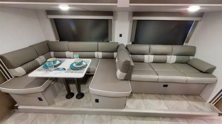 This RV rental features a modern U-shaped dinette with gray and white seating, a white table set for two, and dark window shades. Ideal for relaxing.. Forest River Wildwood X-Lite 2024