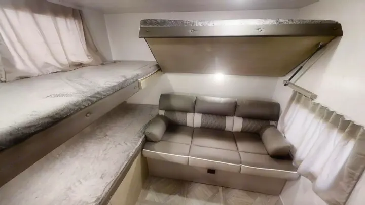 RV rental interior showcasing cozy bunk beds, a sofa, and a space-saving fold-down bed or storage.. Forest River Wildwood X-Lite 2024