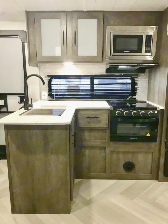 RV rental kitchen: stylish dark wood cabinets, white counters, and stainless appliances including microwave, oven, & sink.. Forest River Wildwood X-Lite 2023