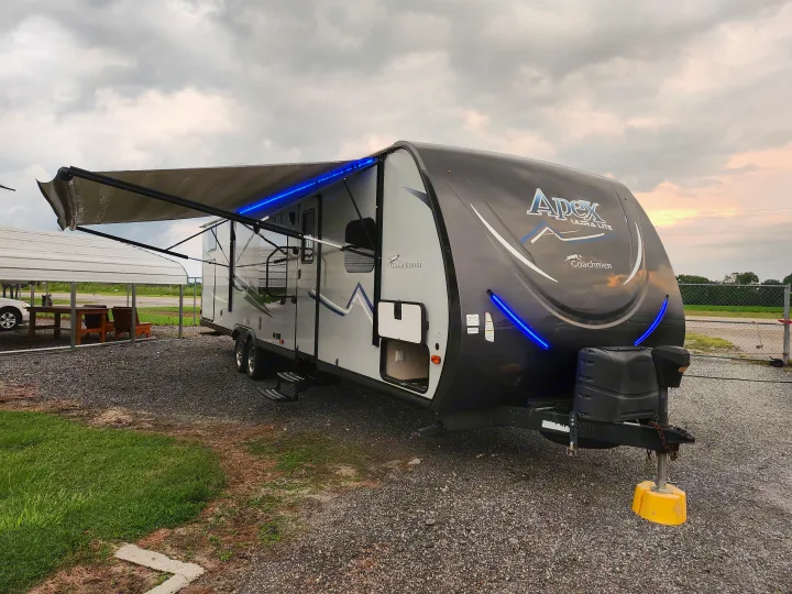 An Apex Ultra Lite RV rental, with its awning extended and bright blue LED lights, is parked on a gravel lot.. Coachmen Apex 2017