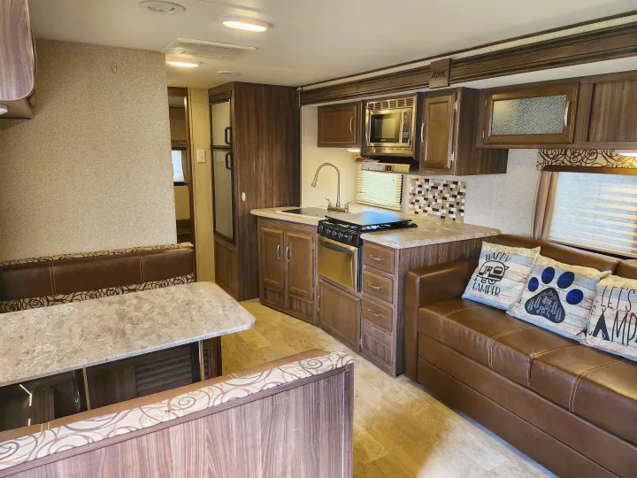 Modern rv rental interior: full kitchen with stove, microwave, and ample cabinets, plus dining booth and comfy sofa.. Coachmen Apex 2017