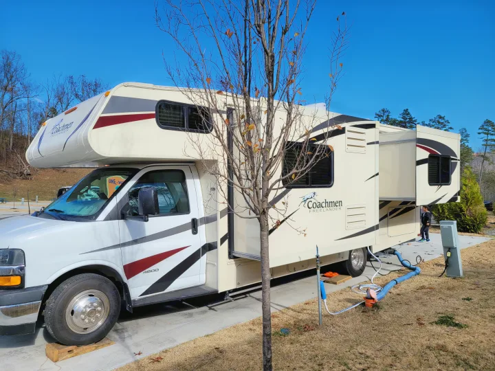 A white Coachmen Freelander rv rental at a sunny campsite, hooked up with slide-out extended. A child is nearby.. Coachman Freelander 2019