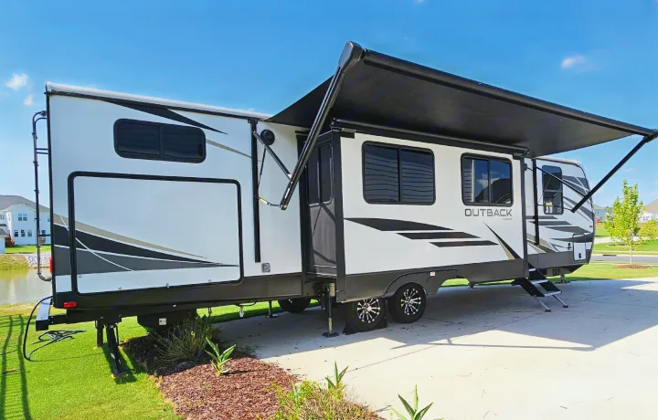 Discover this white travel trailer RV with extended awning and steps, ideal for your next RV rental adventure. Parked on a sunny day.. Keystone RV Outback 2021