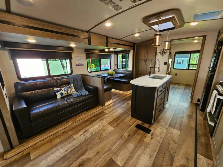 Explore this comfy RV rental interior: spacious living area with a sofa, dining booth, and full kitchen island. Your cozy home on wheels!. Keystone RV Outback 2021