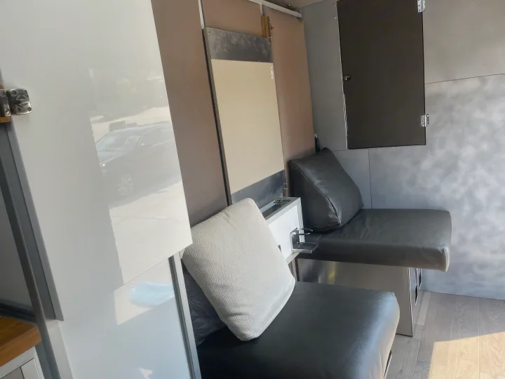Modern RV rental interior with black bench seating, light walls, wood-look floor, and a car reflection from a window.. Other Transit 2022