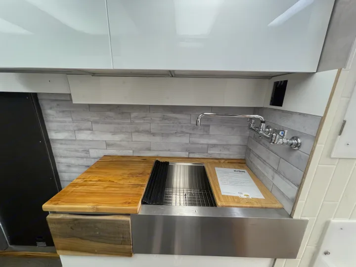 Sleek RV rental kitchen featuring a stainless steel sink, custom wood counter, and modern tile backsplash.. Other Transit 2022