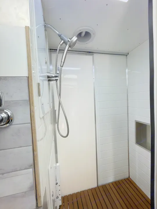 Bright, modern RV rental shower featuring white subway tiles, chrome fixtures, a built-in niche, and a warm slatted wood floor.. Other Transit 2022