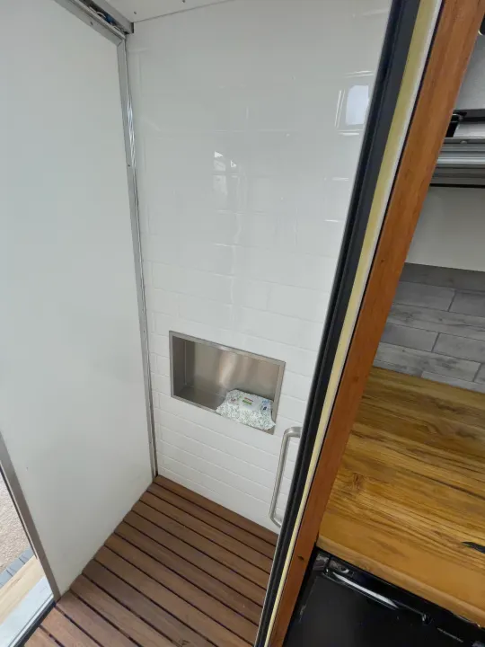 RV rental shower interior with white subway tiles, a slatted wood floor, and a built-in niche holding baby wipes.. Other Transit 2022