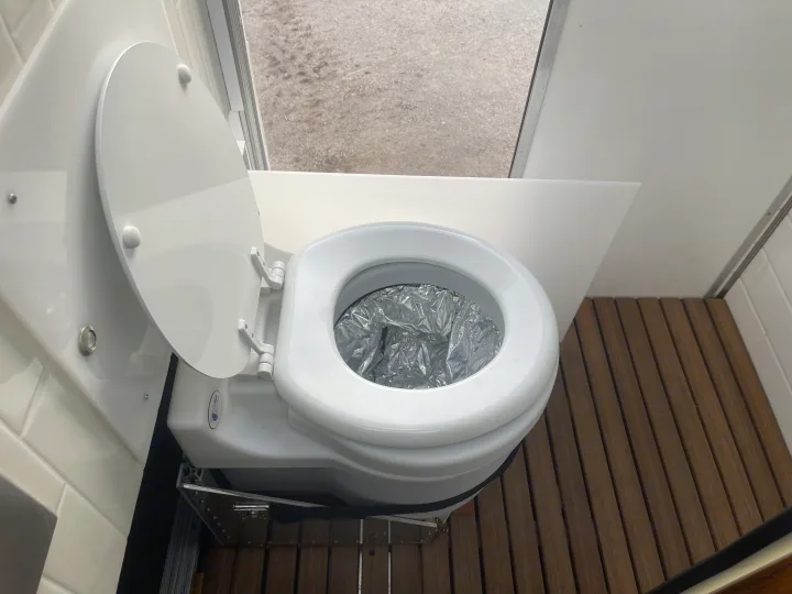 Clean composting toilet in an **rv rental**, ready for your trip. Features a silver liner, wooden floor, and white interior.. Other Transit 2022