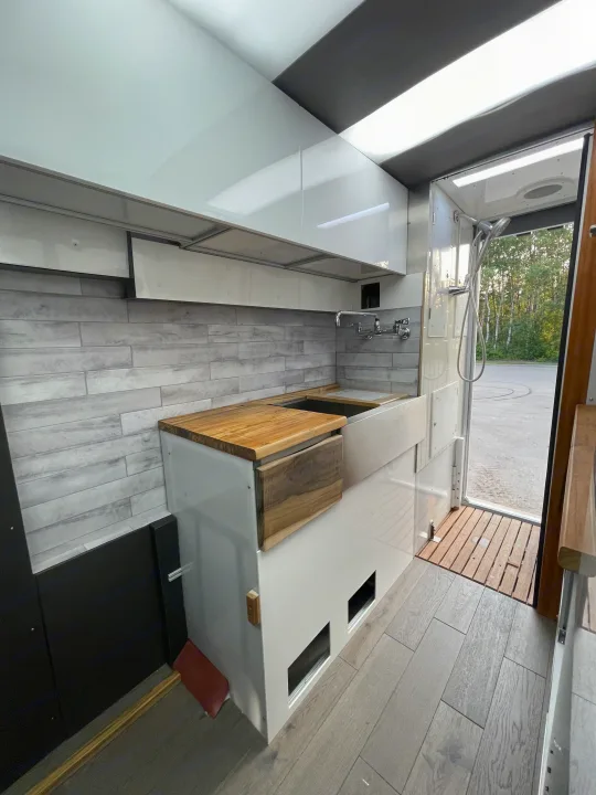 Bright RV rental interior with a sleek kitchen, tiled backsplash, wooden counters, and a convenient shower by the exit.. Other Transit 2022