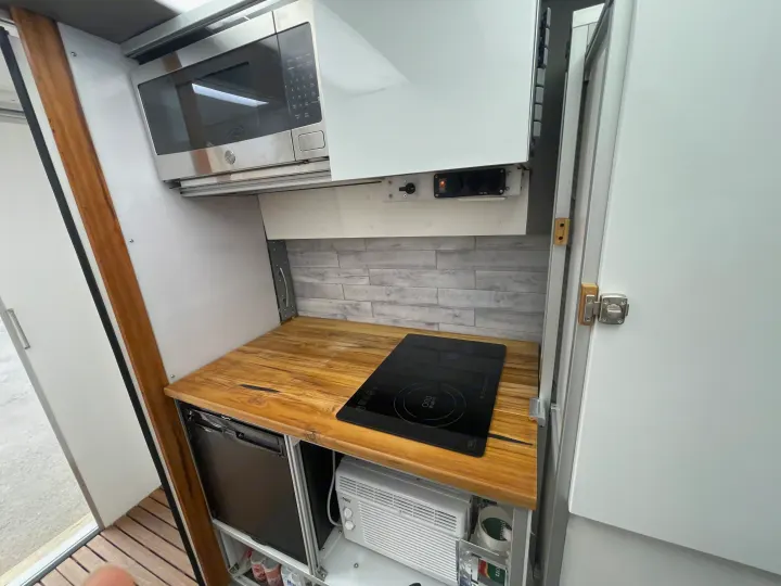 This compact RV rental kitchen features a microwave, induction cooktop, fridge, and wooden counter, ideal for mobile living.. Other Transit 2022