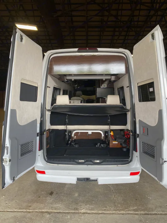 Inside an RV rental: Rear view of a white camper van with open doors, showing its versatile interior, convertible bed, and storage.. Airstream Interstate 2016