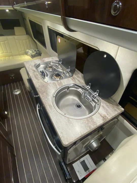 Interior of an RV rental showing a compact kitchenette with a stainless steel sink, dual-burner stove, and light-colored seating.. Airstream Interstate 2016