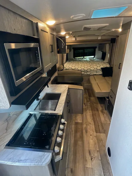 Cozy rv rental interior with a full kitchen (microwave, stove, sink), dining/lounge area, and a comfortable bedroom. Ideal for travel.. Keystone RV Outback Ultra-Lite 2021