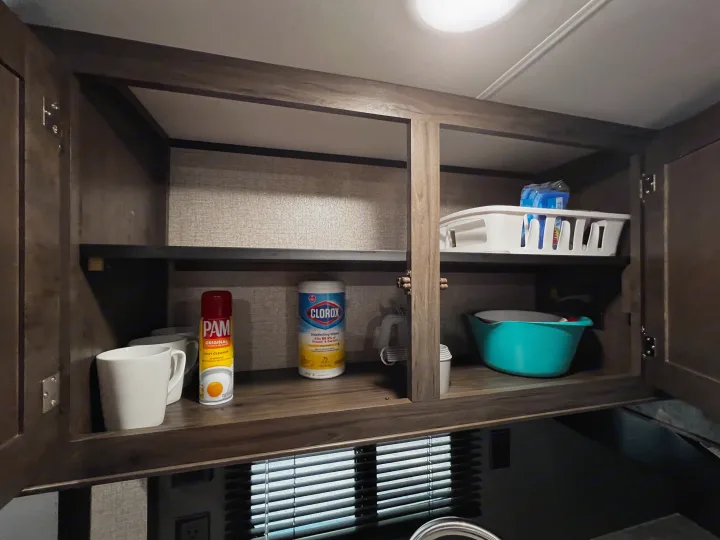 An organized RV rental kitchen cabinet stocked with PAM, Clorox wipes, mugs, and a turquoise bowl, ready for use.. Jayco Jay Flight 2021