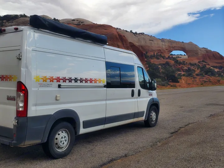 Scenic RV rental: A white camper van beside a natural rock arch and red rock formations.. Custom Camper 2017