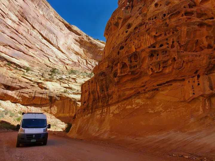 White RV rental on a dirt road through a towering red rock canyon with intricate formations, under a clear blue sky.. Custom Camper 2017
