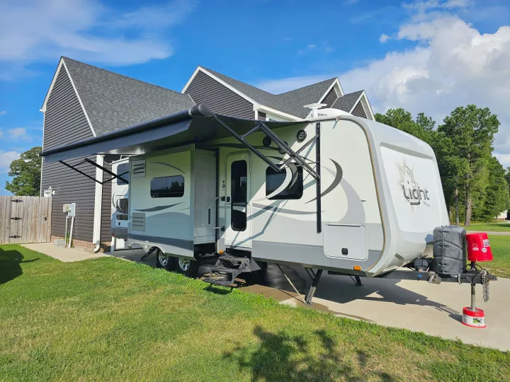 Spacious RV rental parked alongside a modern house with an extended awning in sunny weather.. Open Range RV Light 2014