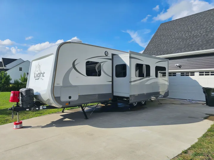 This RV rental is set up in a home driveway with its slide-out extended, ready for adventures or temporary living.. Open Range RV Light 2014