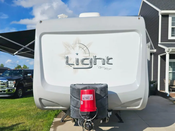 Front view of an RV rental, a Light by Open Range travel trailer, parked on a driveway. A red bucket covers the hitch.. Open Range RV Light 2014
