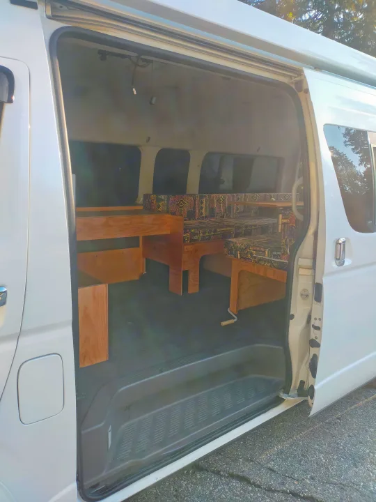 Inside an RV rental camper van, featuring a custom wood interior with built-in bed/seating and patterned cushions.. Toyota Hiace 2005