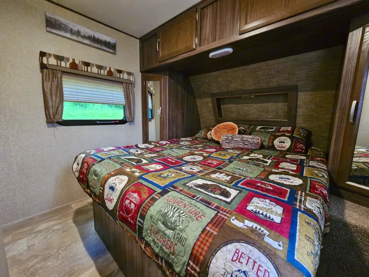 Cozy RV rental bedroom featuring adventure-themed bedding, log pillows, and ample storage. Perfect for a travel escape.. Coachmen Apex 2017