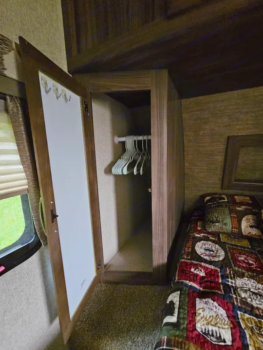 RV rental bedroom: Open closet with hangers, hooks on door, and a comfy bed with a patterned quilt, maximizing space.. Coachmen Apex 2017