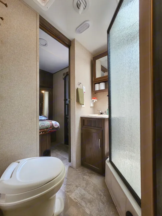 RV rental bathroom showing a toilet, sink, and shower, with a view into the bedroom. Highlights the compact interior.. Coachmen Apex 2017