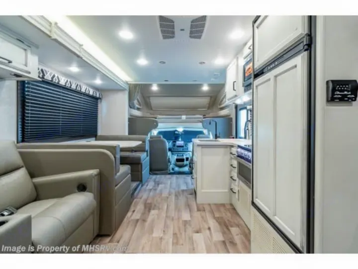 Interior view of an RV rental showing a light-toned kitchen, dinette, living area with recliner, and wood-look floor.. Entegra Coach Odyssey 2021