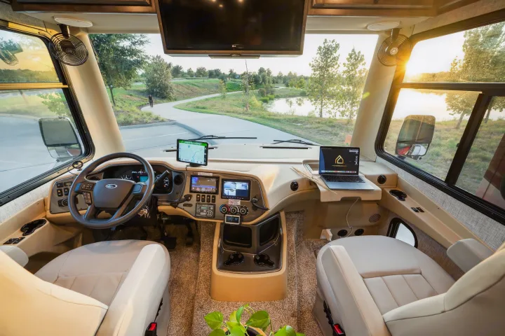 Inside a comfortable RV rental, featuring the driver's cockpit, dashboard, and a bright view of a scenic park.. Tiffin Open Road 36UA 2023