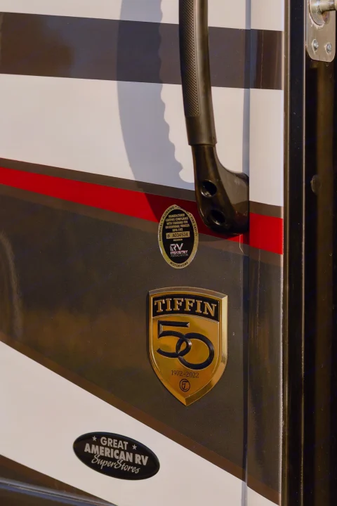 Detail of a Tiffin RV's side with a grab handle and golden 50th-anniversary emblem (1972-2022), certified by RVIA. Great for rv rental.. Tiffin Open Road 36UA 2023