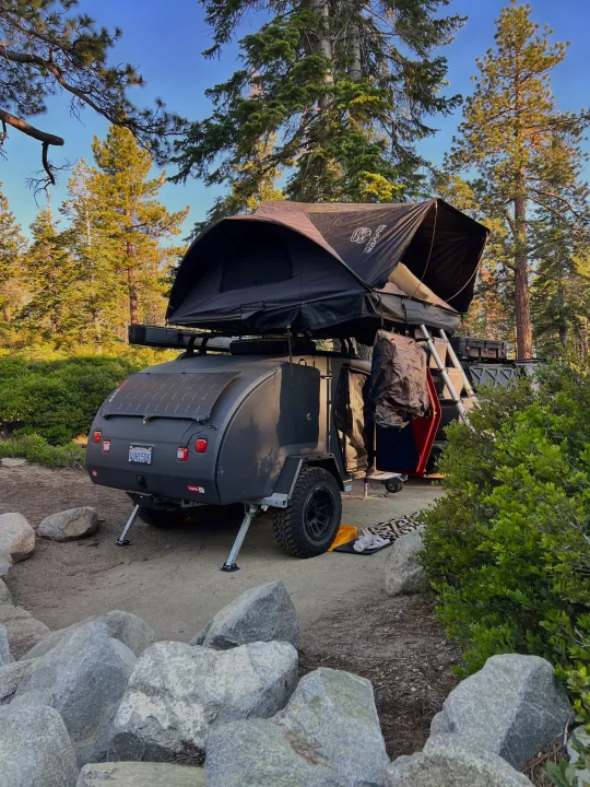 RV rental ready for adventure: dark grey teardrop trailer with rooftop tent set up in a sunny forest camp.. Escapod Escapod Trailer 2023