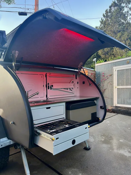 Ready for adventure, this rv rental teardrop camper reveals its illuminated outdoor kitchen with a sink, pull-out stove, and fridge.. Escapod Escapod Trailer 2023