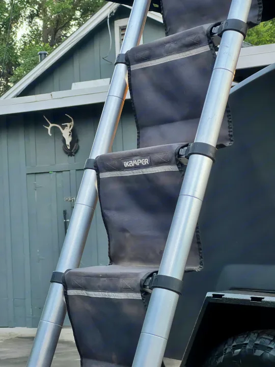 Extending iKamper ladder and dark gray RV rental unit. Steps are fabric, poles aluminum. Deer skull on building nearby.. Escapod Escapod Trailer 2023