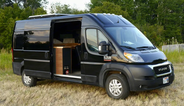 Black Ram ProMaster campervan with open side door, showcasing its converted interior. Ideal RV rental for outdoor adventures.. Ram Promaster 2019