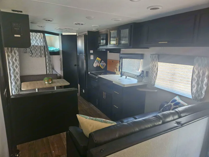 Inside an RV rental, showcasing the compact kitchen, dining nook, comfy sofa, and bunk beds. Modern and functional space.. Forest River Cherokee Grey Wolf Special Edition 2022