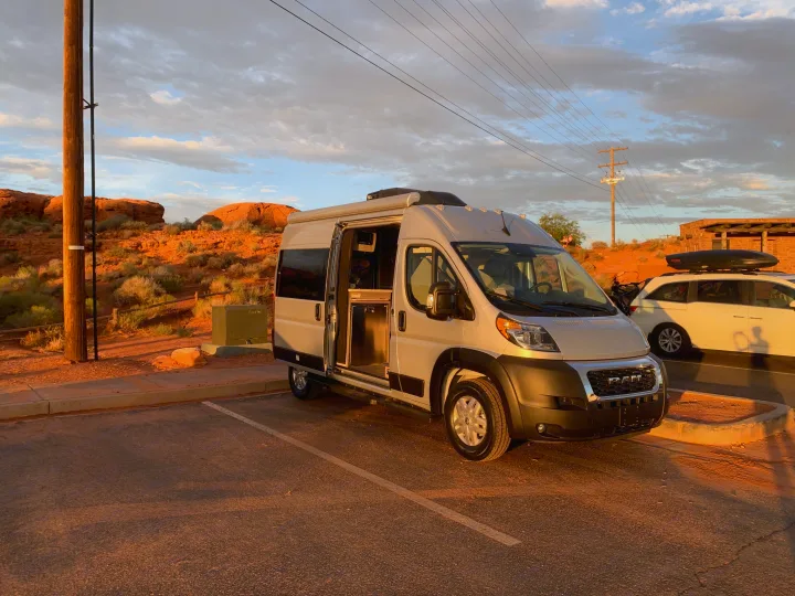 RV rental camper van parked with open side door, showcasing its interior against a scenic red rock desert sunset.. Thor Motor Coach Scope 2023