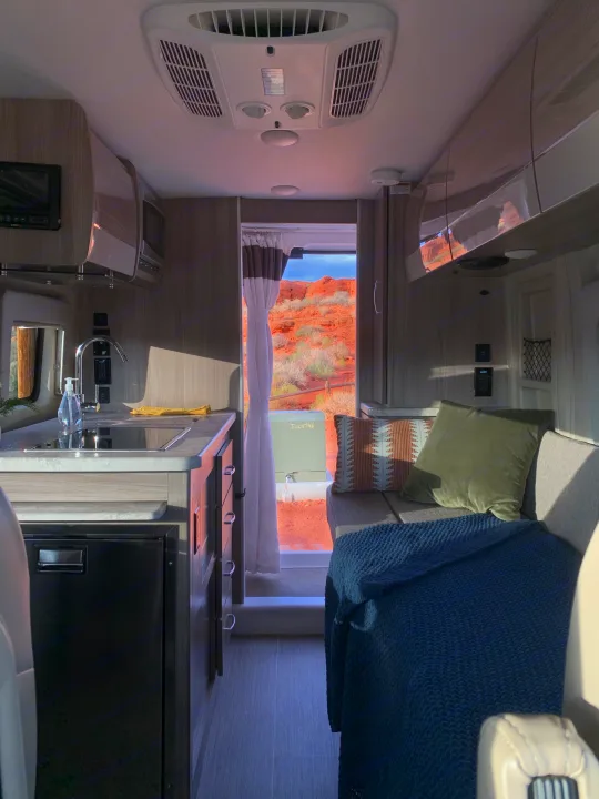 An inviting RV rental interior with a modern kitchen, cozy seating area, and a striking red rock desert view through the rear door.. Thor Motor Coach Scope 2023