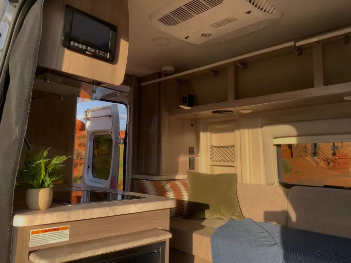 Inside an rv rental: a cozy camper van interior with kitchen, couch, and open back door offering desert views.. Thor Motor Coach Scope 2023