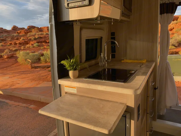 RV rental: Bright kitchenette in a modern RV, featuring a sink, stovetop, and clear views of a sunny red rock desert landscape.. Thor Motor Coach Scope 2023