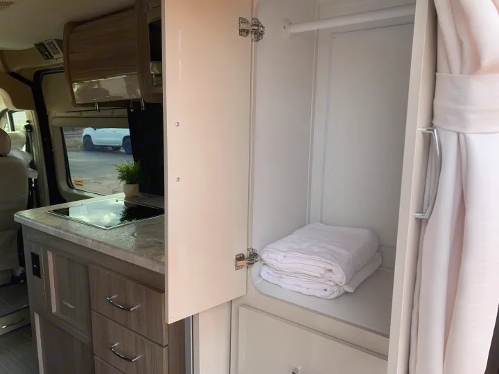 RV rental interior showing a clean kitchenette with cooktop and an open wardrobe with fresh towels.. Thor Motor Coach Scope 2023