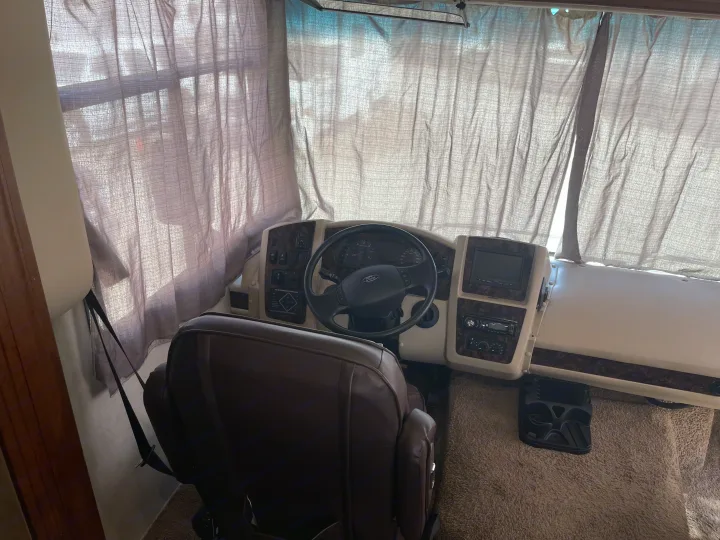 RV rental cockpit view: brown driver's seat, Ford steering wheel, and dashboard. Front curtains are drawn for privacy.. Coachmen Pursuit 2014